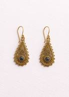 A pair of ornate gold-toned filigree dangle earrings with scalloped edges and a small round dark blue-gray stone at the centre of each earring, shown on a textured off-white background.