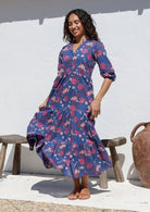 Model stands in sun wearing a navy blue 3/4 sleeved floral cotton maxi dress featuring burgundy, pale pink and plum florals 