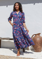 Woman stands with hand in pocket wearing a tiered cotton maxi dress with mandarin collar, buttoned bodice and 3/4 sleeves