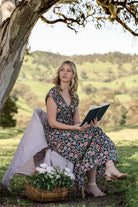 Model sitting with book open in hands wearing 100 percent rayon floral maxi dress