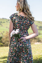 Back view of model holding flowers wearing 100 percent rayon floral maxi dress 