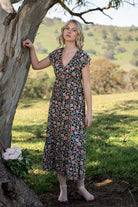 Model leaning on a tree wearing 100 percent rayon floral maxi dress with pockets