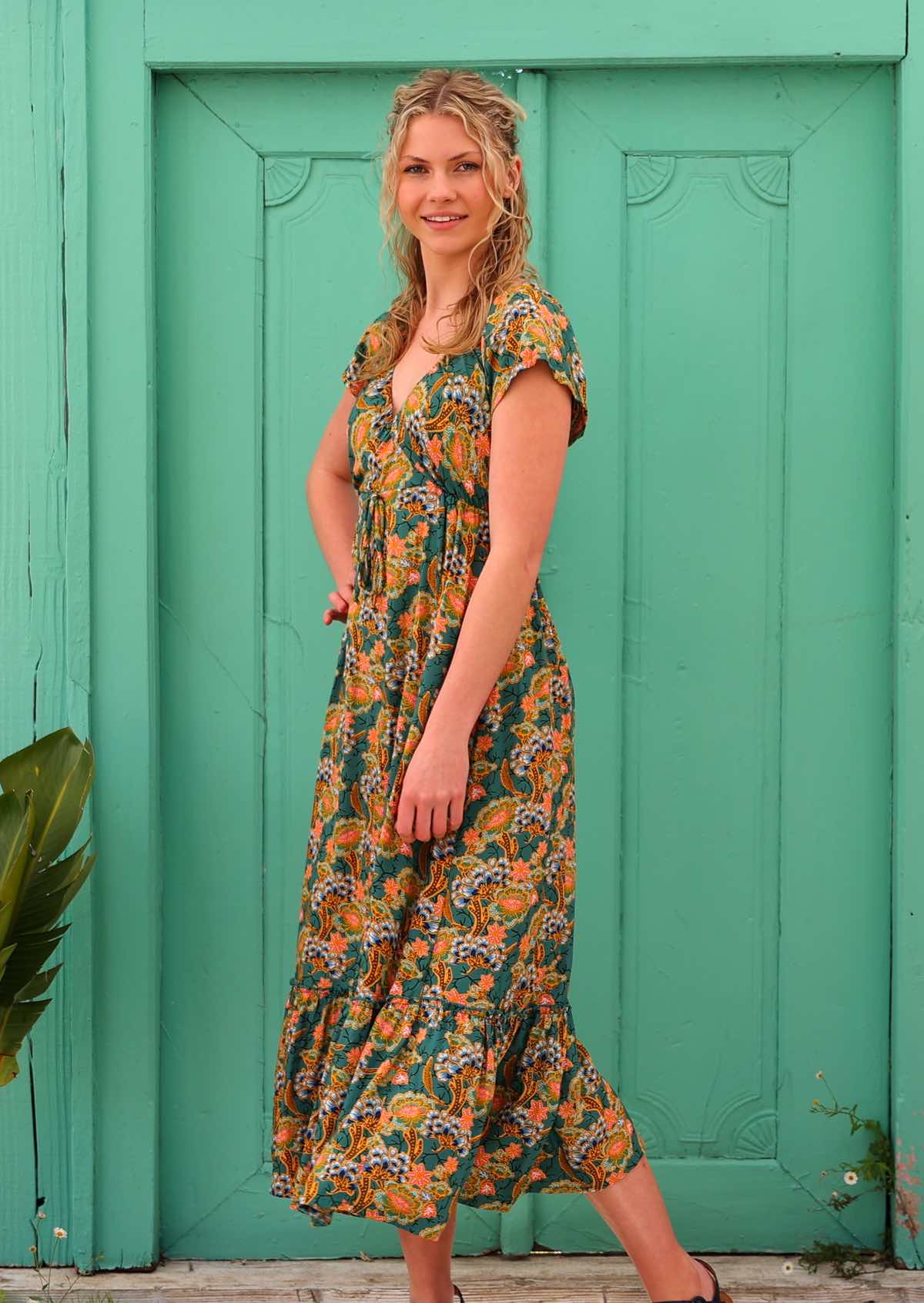 Model with hand on hip standing infront of aqua door wearing 100 percent short sleeve  v-neck rayon maxi dress 