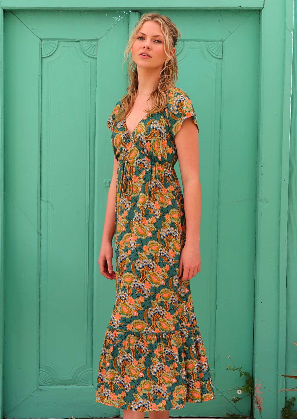 Model standing infront of aqua door wearing 100 percent rayon maxi dress in green based floral print