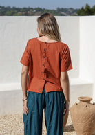 Model wearing a plain rust shade top with non functional buttons down the back