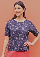 Model poses in cotton T-shirt sleeve top with round neckline in sweet pink, teal and purple floral print on a dark base