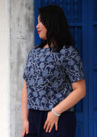 Model standing side on wearing floral navy blue boxy blouse 100 percent cotton with one thumb in pant pocket