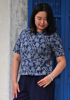 Model looking down wearing floral navy blue boxy blouse 100 percent cotton, thumb in pocket of pants