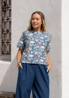 Woman wearing a loose-fit, blue floral 100% cotton boxy top with short sleeves and a seam across the bust
