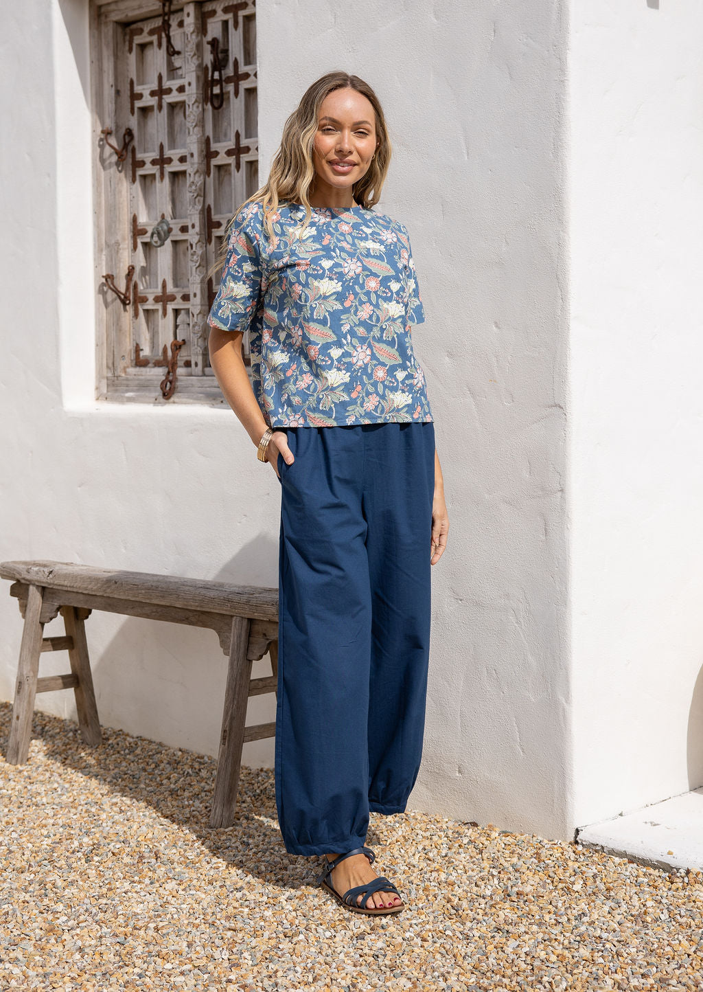 Woman wearing a blue floral cotton boxy top with short sleeves and a high round neckline, paired with dark blue cotton pants.