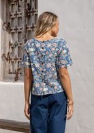 Woman wears a blue floral cotton boxy blouse with non-functional decorative coconut buttons at the back 