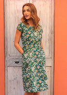 Model standing in front of door with hands in pockets wearing Flannel Flower green floral short sleeve sundress 100 percent cotton 