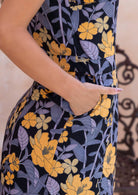 Close up of hand in pocket of retro floral cotton dress with yellow and grey flower prints on a black background 