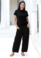 Woman wearing a black t-shirt and black cotton pants in a white villa
