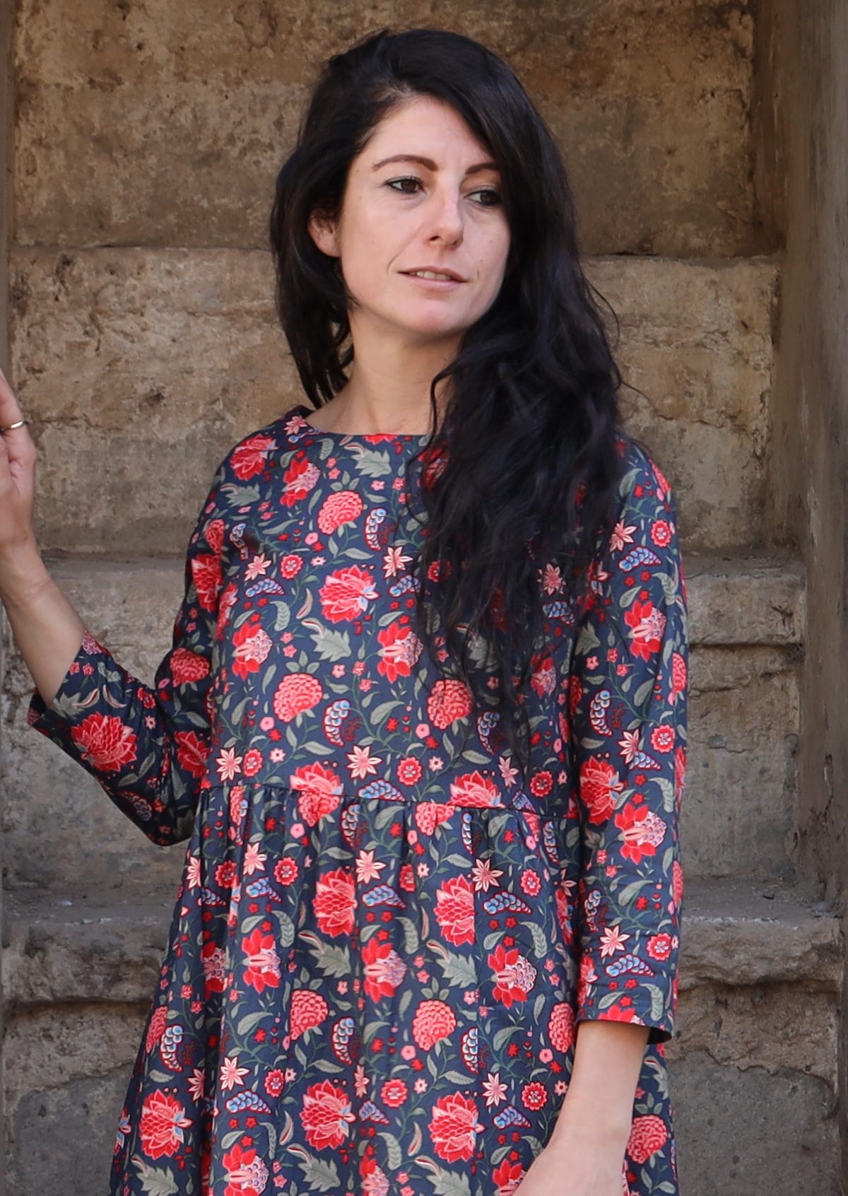 Close up of model with dark hair wearing a 100 percent cotton three tiered blue base and red floral print midi length dress 