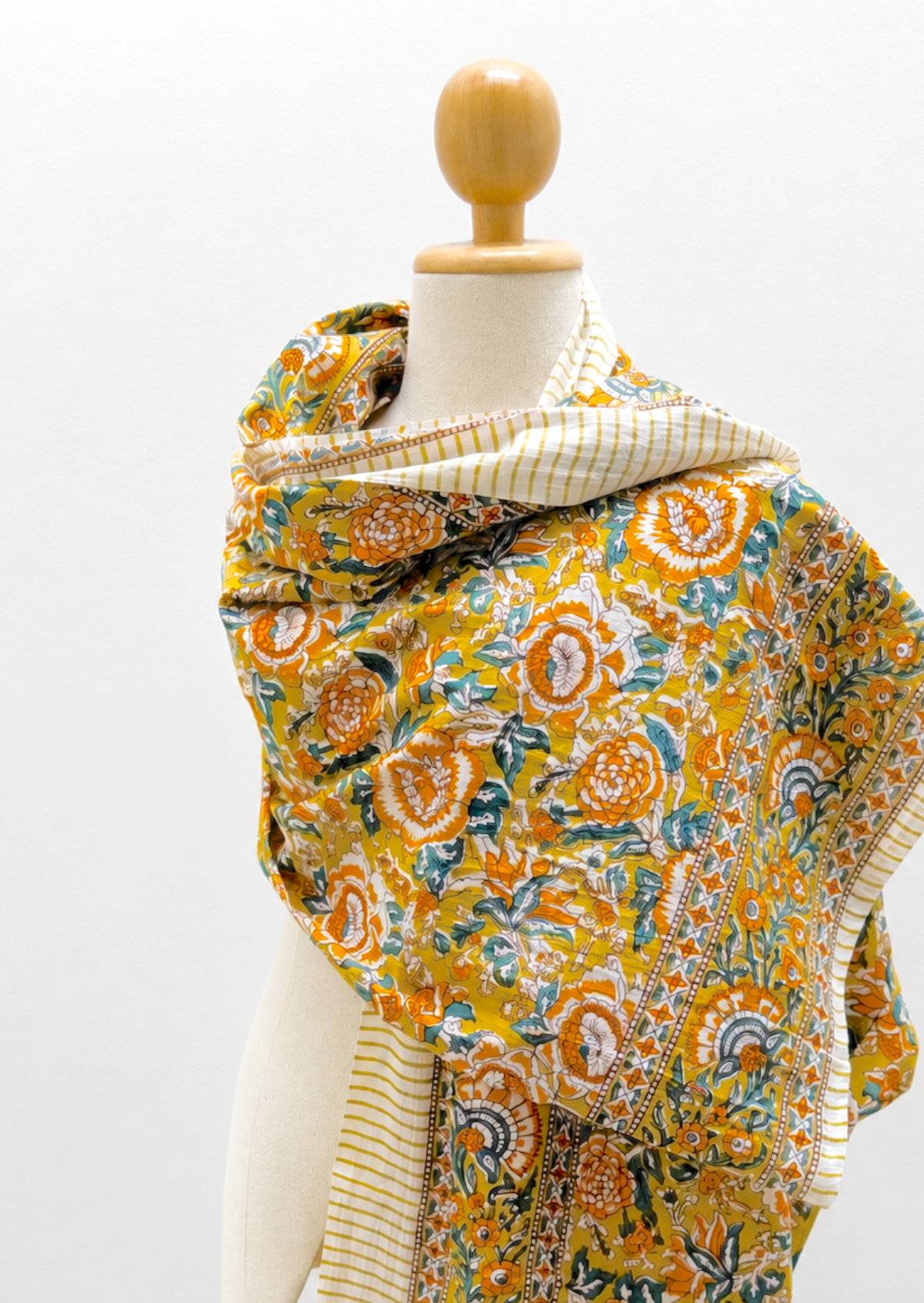 A mustard yellow patterned shawl draped on a cream-colored mannequin torso against a white background.
