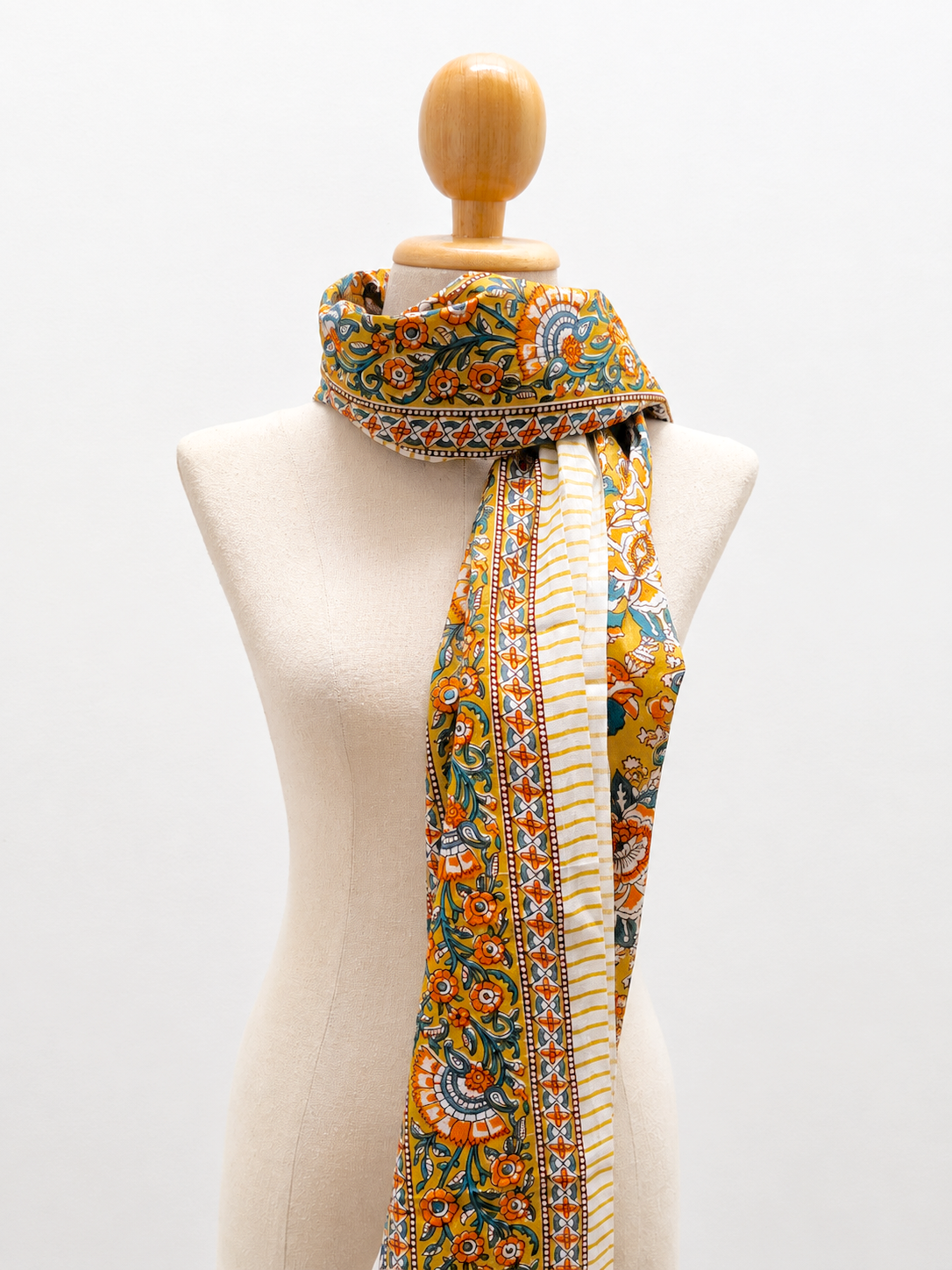 A multicolor patterned scarf with a cream center stripe and embroidered borders, draped on a beige fabric mannequin torso against a white background.