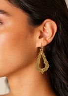 Close up of a woman wearing an elegant gold coloured teardrop shaped earring that has layered rope like detailing, tiny raised bead accents, and small leaf motifs inspired by traditional Indian jewellery