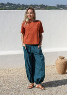 Woman wears relaxed fit lightweight deep teal cotton harem pants with pockets paired with a rust top