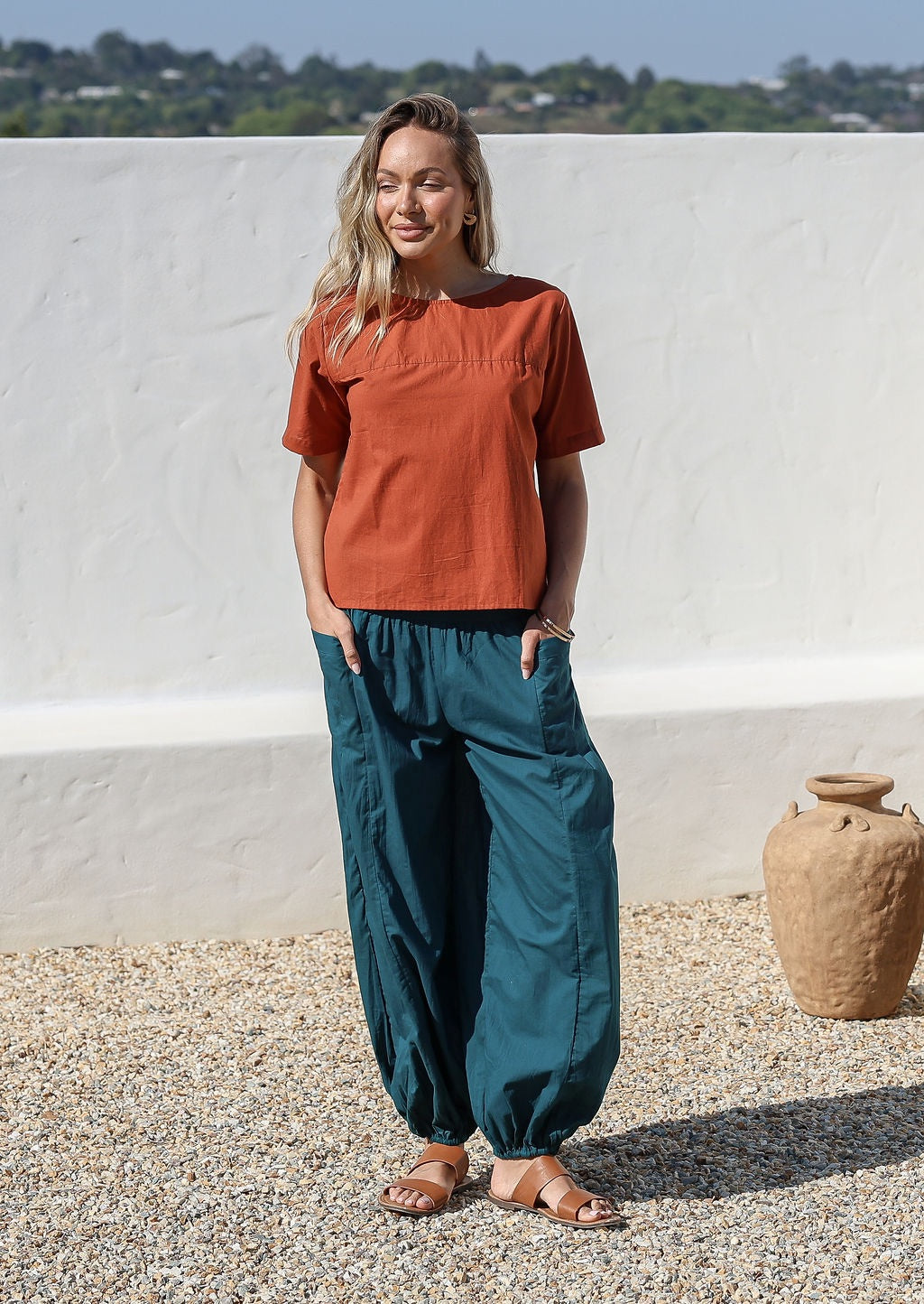 Woman wears relaxed fit lightweight deep teal cotton harem pants with pockets paired with a rust top