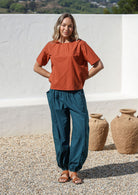 Woman wears wide waistbanded cotton harem pants with a rust short sleeve top 