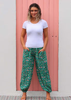 Woman stands in cotton harem style floral pants with elasticated ankles, with her hands in deep pockets