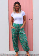 Woman poses in lightweight cotton floral harem style pants with hands in deep pockets