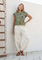 Woman wears relaxed fit lightweight white cotton harem pants with pockets paired with a green floral top