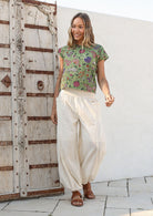 Woman wears wide waistbanded cotton harem pants with a green floral top and brown sandals