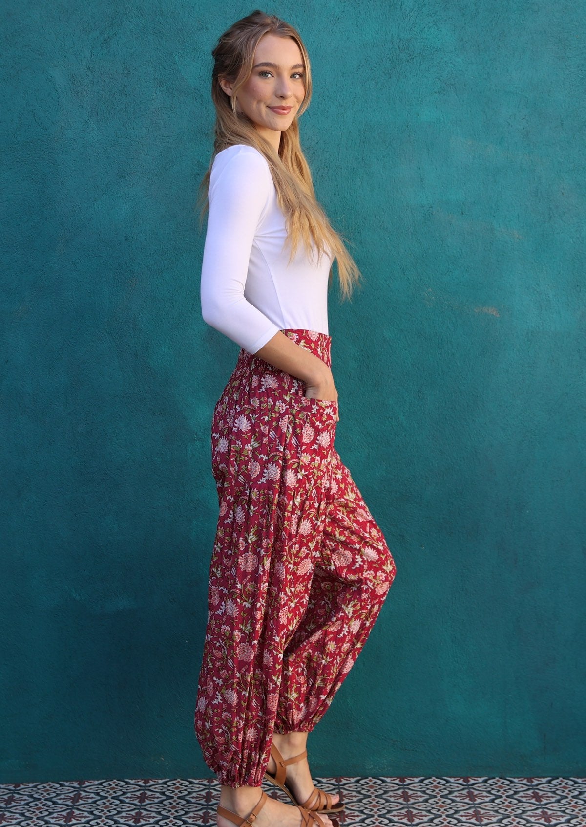 Model standing sideways is wearing a beautiful cotton pants in cranberry base with hands in pockets.