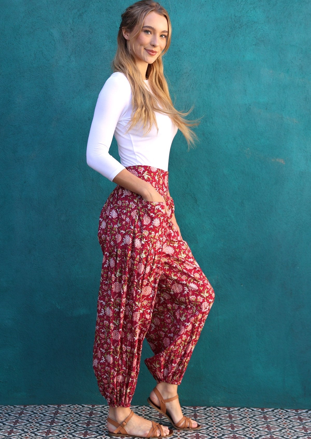 Woman poses in lightweight cotton floral harem style pants with elasticated waistband and hands in deep pockets.