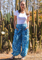 Woman stands in blue floral print cotton harem pants with a wide waistband paired with a white stretch scoop neck rayon top