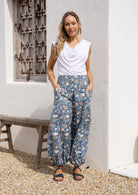 Model standing in sun wearing a relaxed fit, boho cotton pants with lemon yellow, pink and green florals on a blue base.