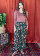 Model stands in 100% cotton harem pants in pink, orange and cream florals on deep green base.