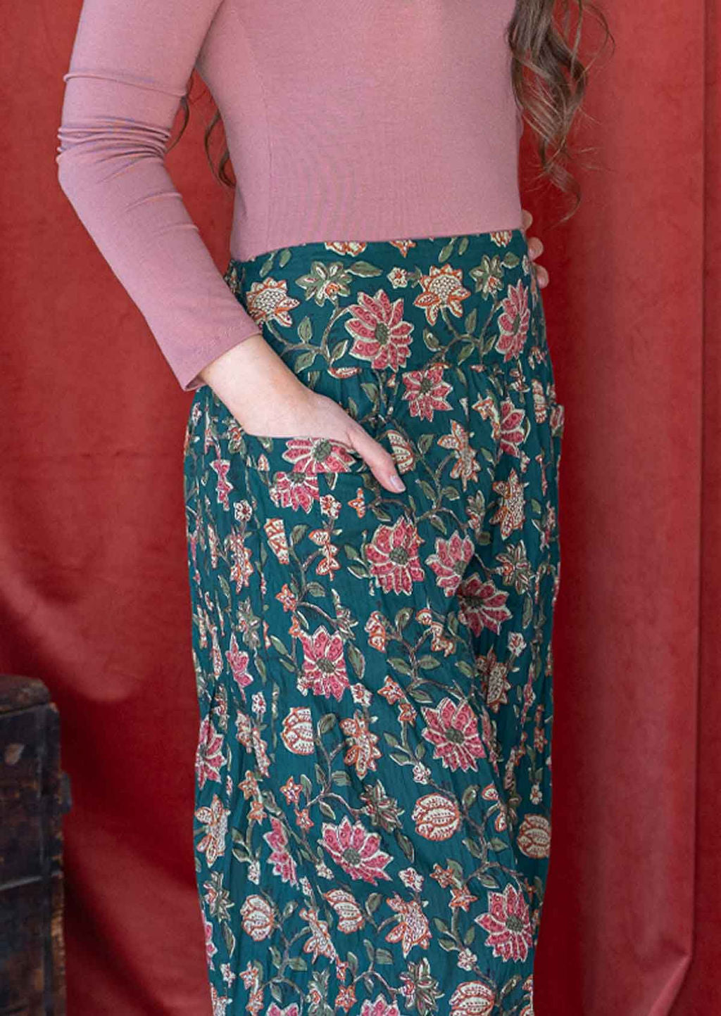 Close up image of a model wearing green cotton harem pants with wide waistband and hand in pocket.
