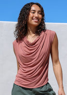 Woman wearing a pink sleeveless top with cowl neck against a blue sky background