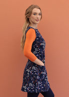 Women posing sideways wears a sleeveless, printed cord tunic with her hand in pocket.