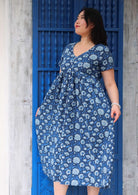 Model holding out skirting of dress wearing 100 percent cotton navy blue button through v-neck dress with pockets