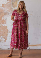 Woman wears 100% cotton button through relaxed fit dress with T-shirt sleeves and V-neckline in floral print on a bright red base