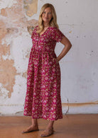 Woman wears lightweight cotton relaxed fit button through floral dress with hand in hidden side pocket