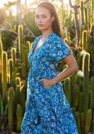  woman in blue cotton floral v neck maxi dress with hands in pocket sun in hair 