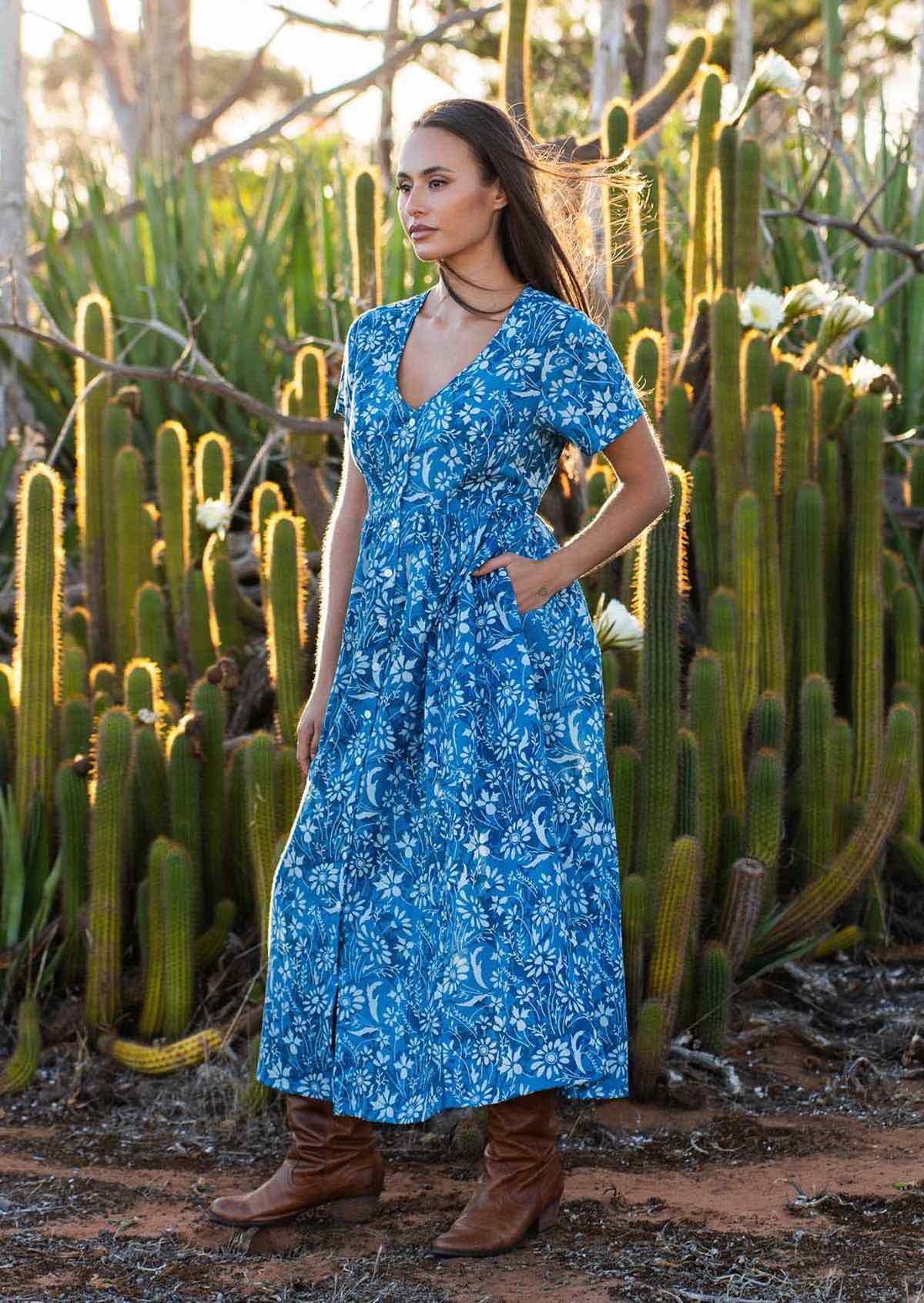 woman in blue cotton floral v neck maxi dress with hands in pocket in field of cacti 