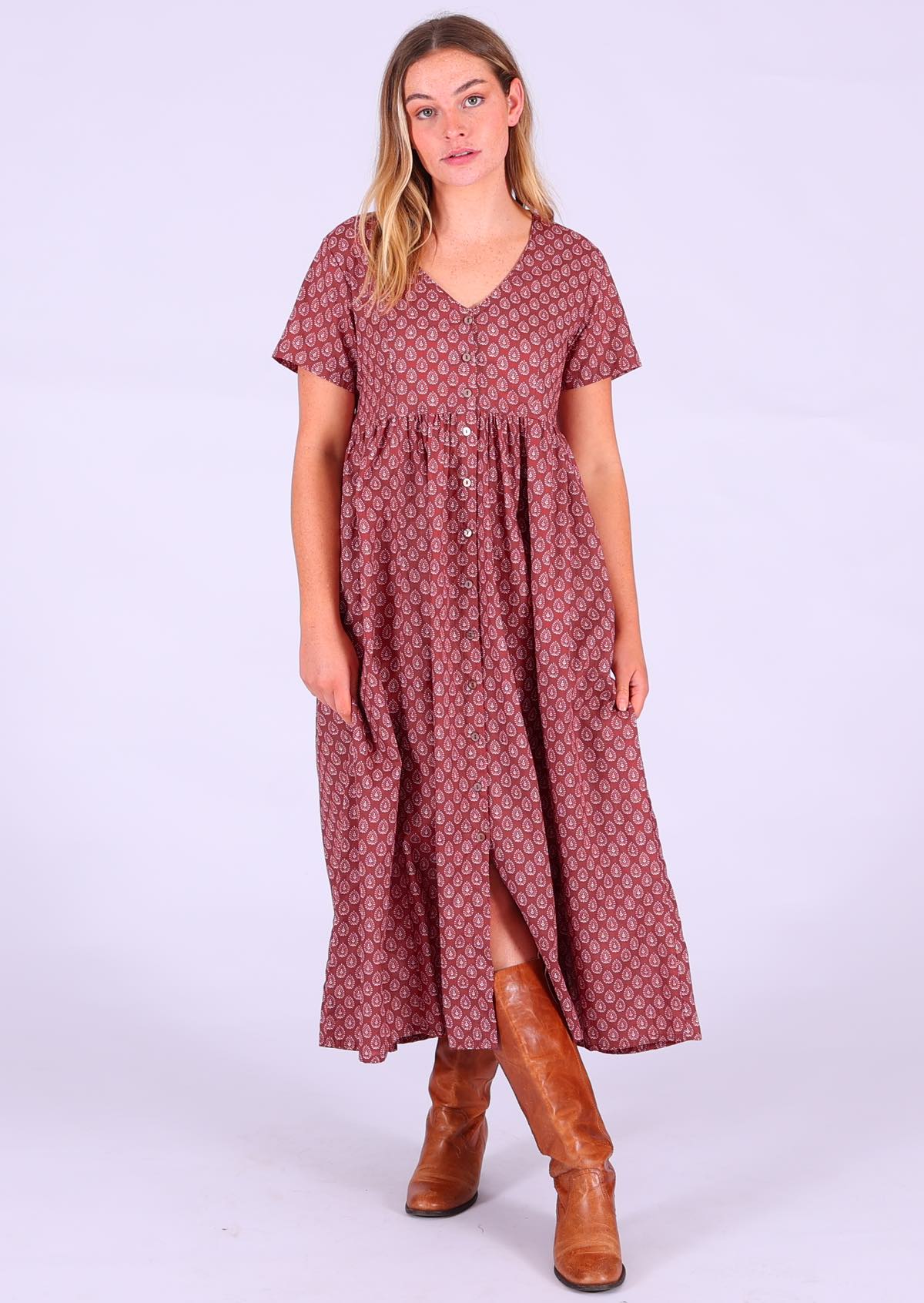 Model standing wearing 100 percent cotton dark terracotta maxi sundress v-neck with pockets paired with tan leather boots 