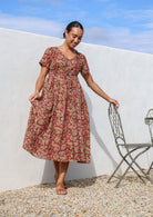 Woman wears lightweight cotton relaxed fit button through red floral dress with  hidden side pocket.