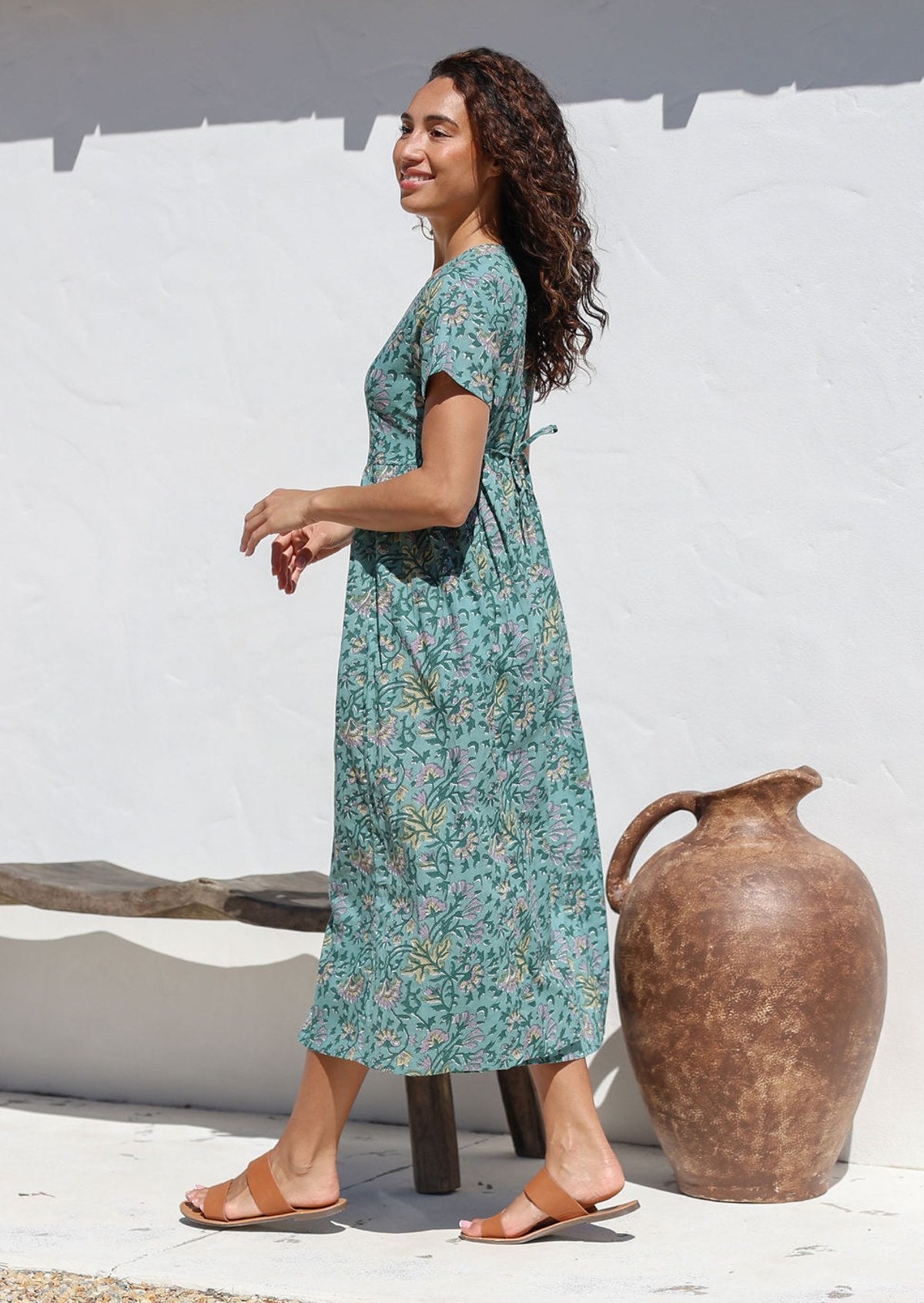 Woman standing sideways wears relaxed fit sage green cotton dress with yellow and grey floral print 