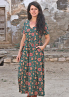 Model standing slightly sideways and smiling with one hand in pocket wearing 100 percent cotton dark jade green button through v-neck dress with pockets