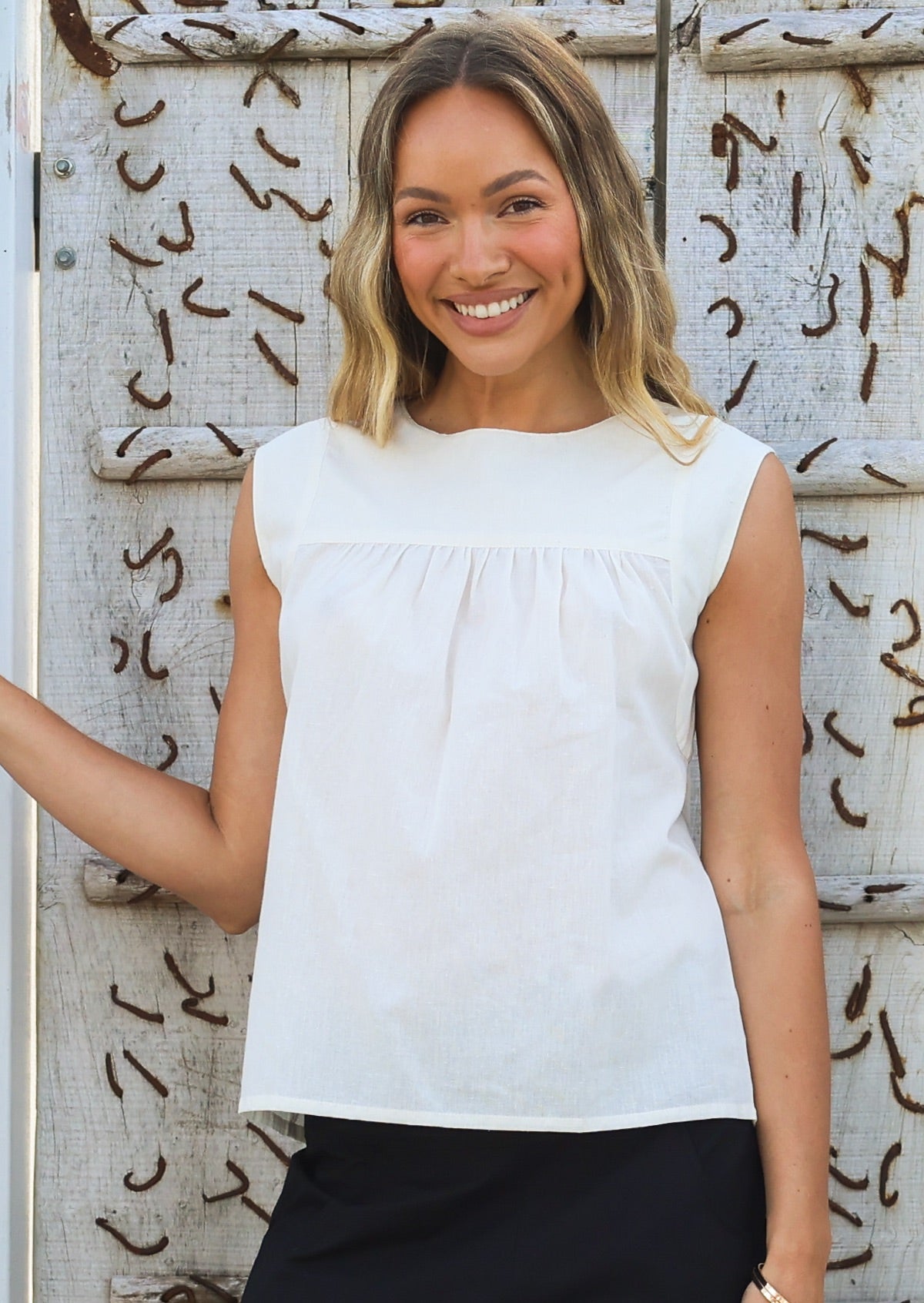Woman wears a natural white cotton sleeveless top with small gathers across the bust