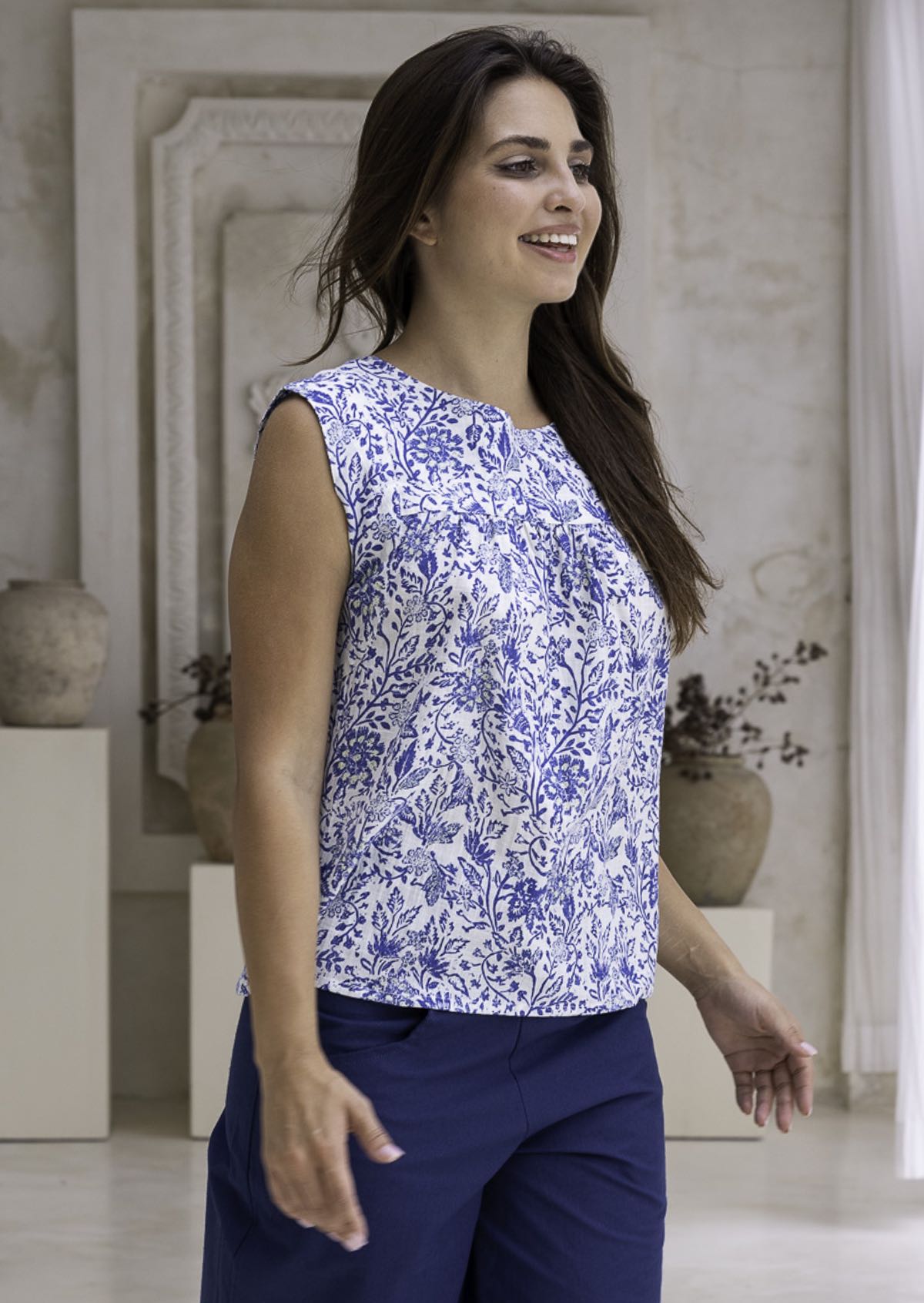 Woman wearing a white based blue floral, loose fit cotton top in an indoor setting.