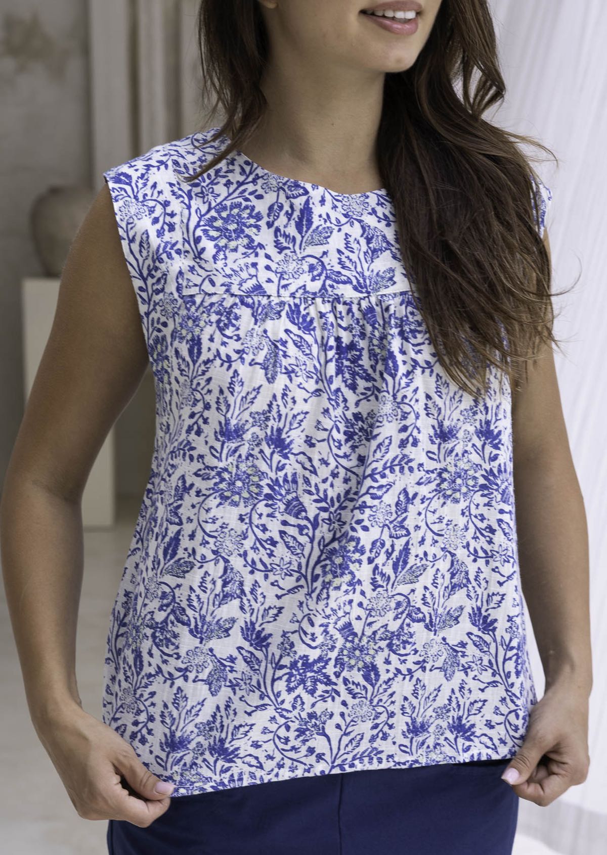 Woman wearing a white based blue floral cotton top with a blurred background.