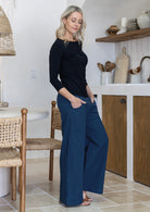 Woman standing side on wearing blue cotton wide leg pants with a wide waistband, side zipper, with hands in pockets